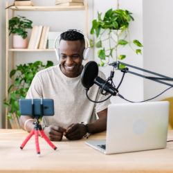 Young adult african man streaming live video at home studio - Millennial content creator male recording radio podcast - Entertainment and broadcasting concept